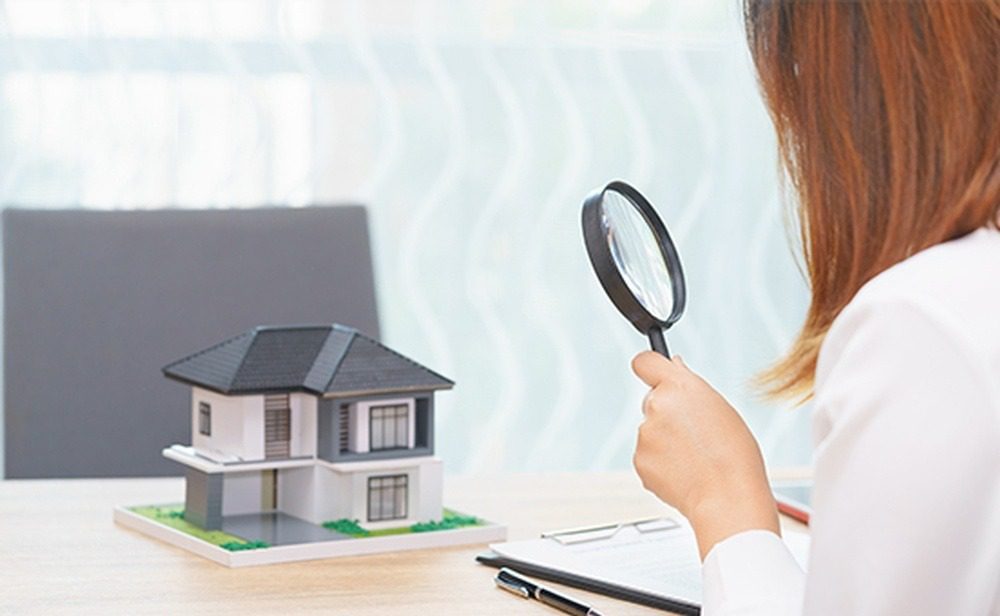 A woman looking at a model house with a magnifying glass.