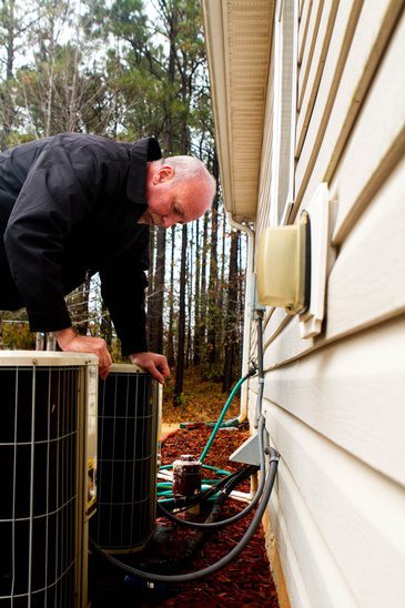 A man inspecting an air conditioner on the side of a house.