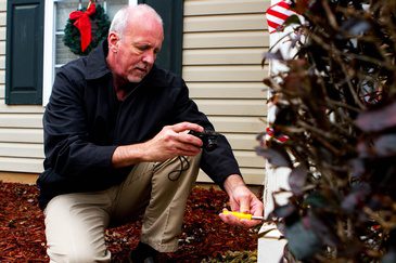 A man kneeling down in front of a house with a christmas tree.