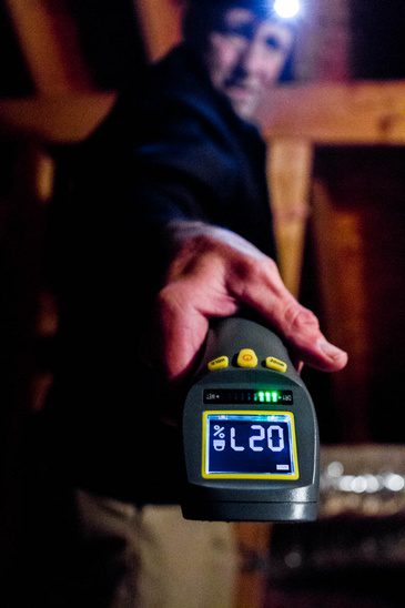 A man holding an infrared thermometer in an attic.