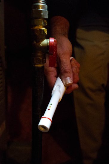 A man is holding a thermometer in front of a pipe.
