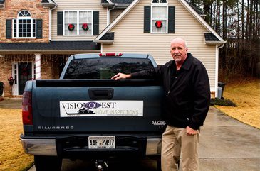 A man standing in front of a house with a truck in front of it.